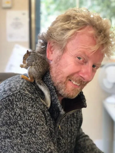Julian, Tidal Drift's founder, smiling with a tame grey squirrel perched on his shoulder.