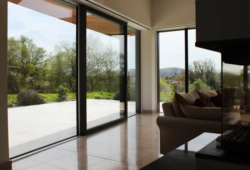 Open-plan living room with full-width sliding doors framing a rural Sussex view, a woodburner and a tiled floor.