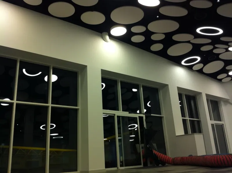 The stadium concourse building at night, its white façade and circular-panelled canopy soffit lit from within.
