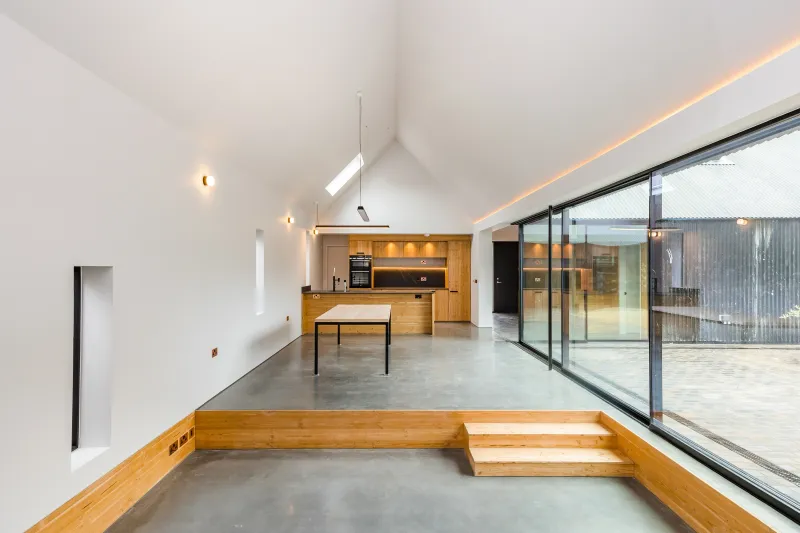 Open-plan living and kitchen space with a vaulted white ceiling, polished concrete floor and sliding doors to a courtyard.