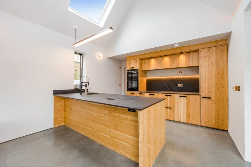 A bespoke timber kitchen with a dark stone worktop and integrated appliances beneath a vaulted ceiling.