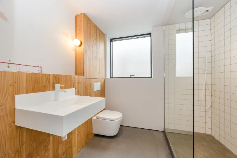 A bathroom with a white basin and wall-hung toilet against timber panelling, beside a tiled shower