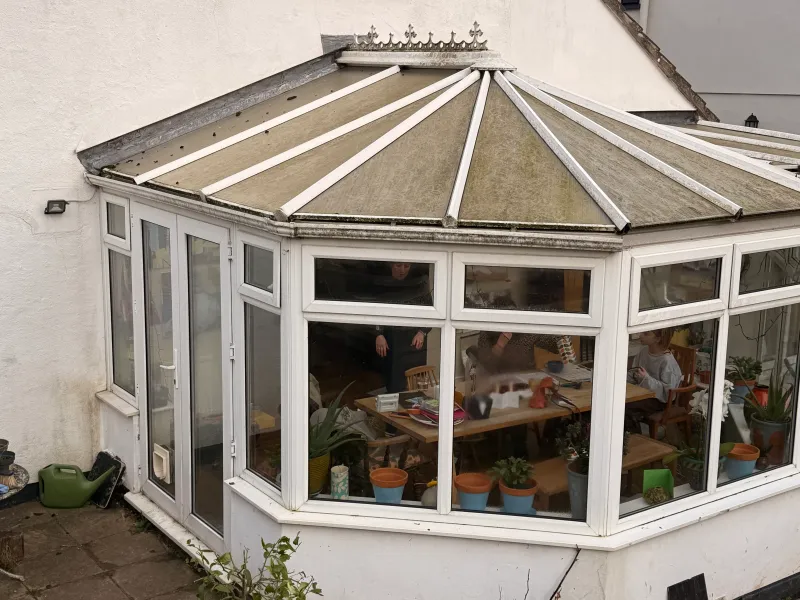 The old 1980s conservatory on the back of the house, with its polycarbonate roof and white PVC frames.