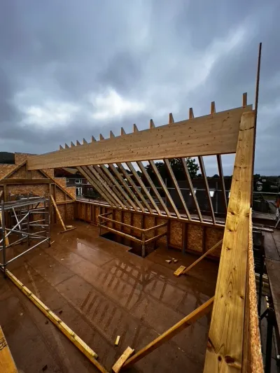 A newly framed mono-pitch roof structure under construction on a wet day, with exposed rafters and scaffolding.