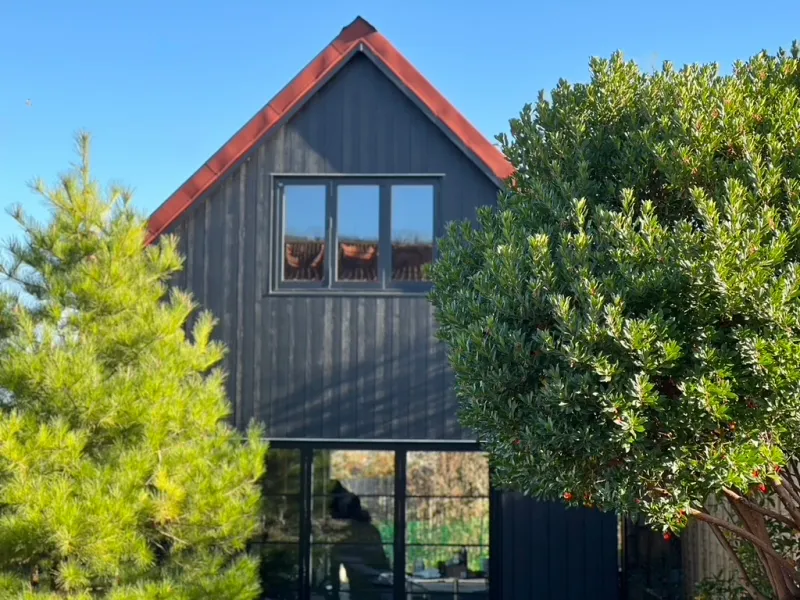 The completed Steyning artist's studio, a dark-clad two-storey building with warm roof trim and large glazing, framed by trees.