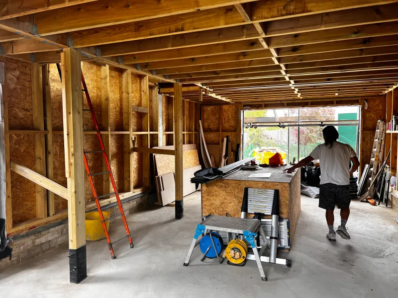 The ground floor of the studio in its timber frame, with a builder at a workbench