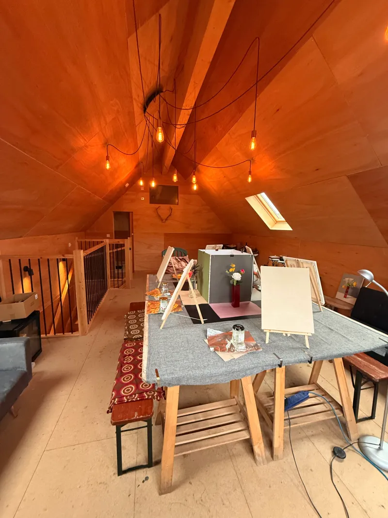 The upstairs studio lined in plywood, with easels and canvases on a long table under hanging lights