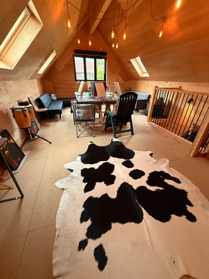 The upstairs studio with a table, chairs, a sofa and a cowhide rug under the roof lights