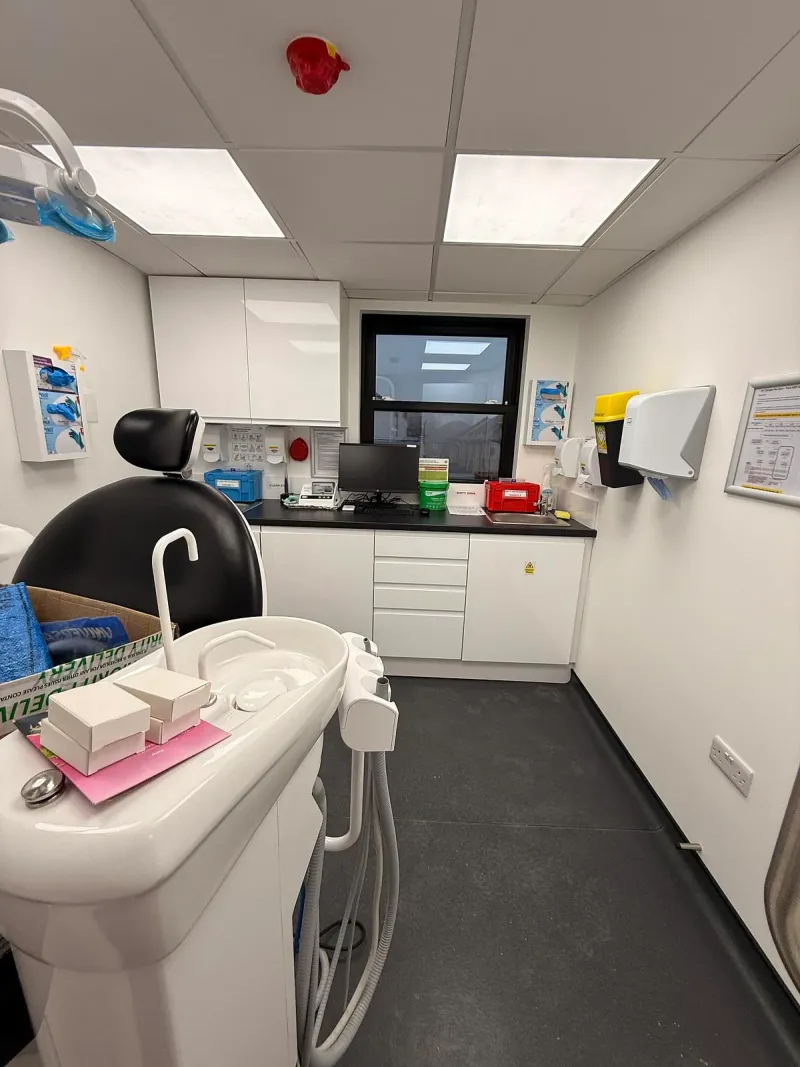 A finished surgery with its dental chair, white cabinets and a window.