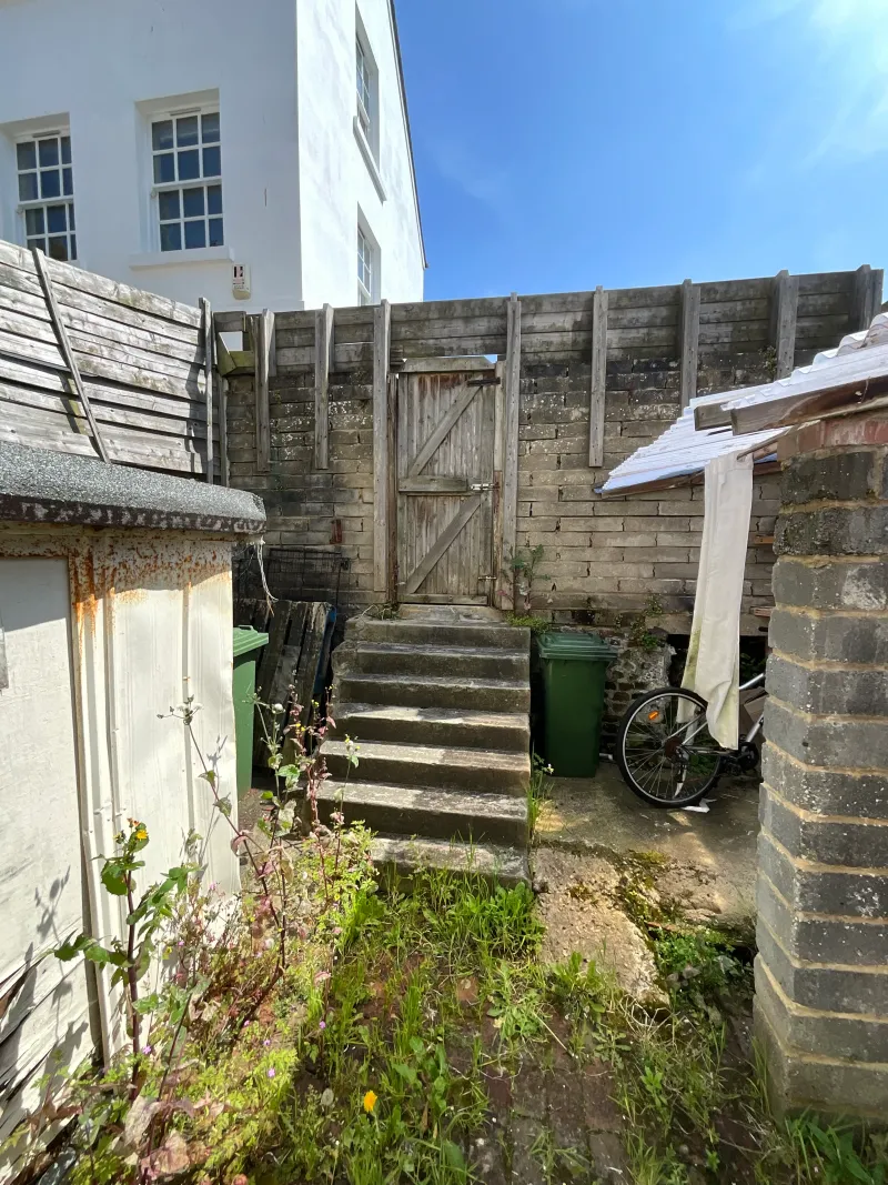 The overgrown back yard, with steps up to the rear gate, before the extension