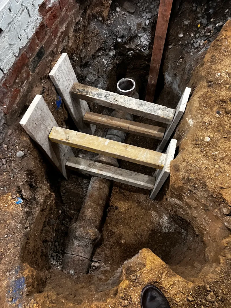 An old pipe at the bottom of a shored trench behind the building