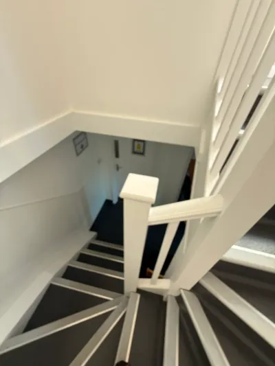 A carpeted domestic-style staircase with a painted balustrade, looking down to the hallway, before conversion.