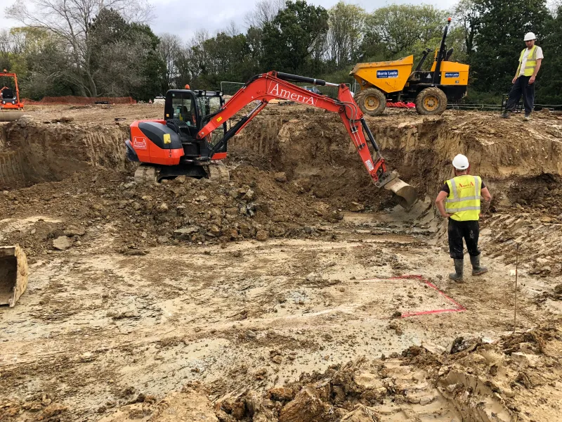 An excavator and dumper at work on the bare site at the start of the groundworks