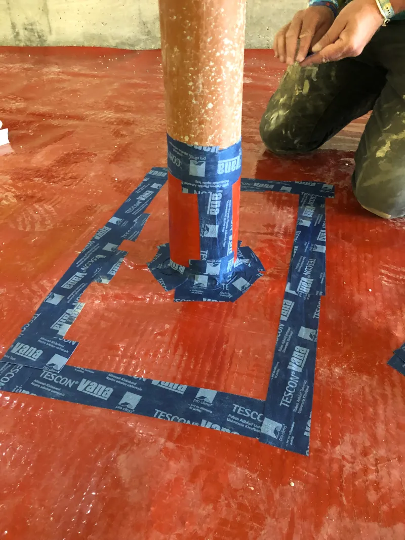Blue airtightness tape sealing a pipe where it passes through the red membrane