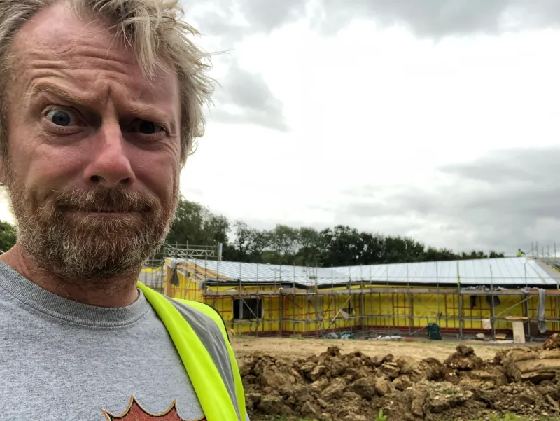 Julian in a high-visibility vest, with the house under scaffolding behind him