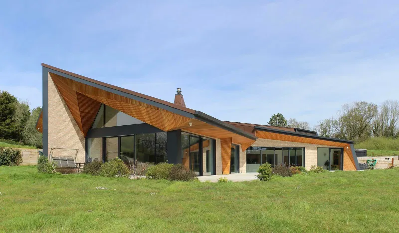 Weald House from the lawn: a folded roof with cedar-lined soffits over pale brick walls and full-height glazing.