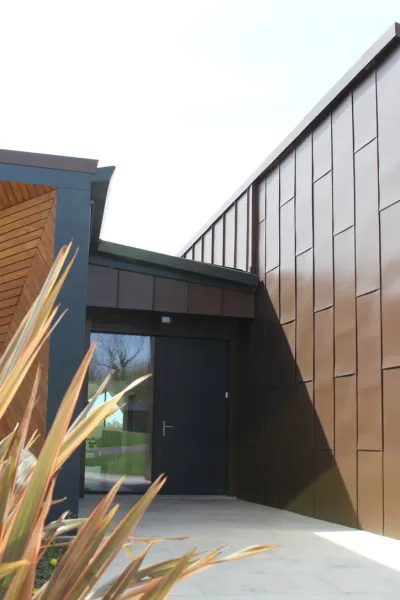 The entrance to Weald House, with bronze standing-seam cladding, a recessed dark door and timber detailing.