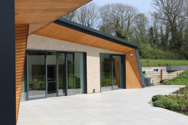 Weald House from its terrace, with timber-lined eaves and a dark fascia over brick, and a large paved patio.