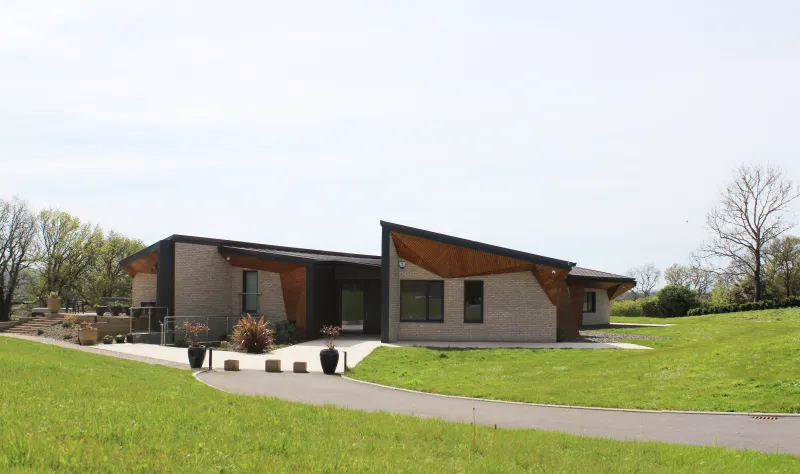 Weald House across its landscaped drive, a long single-storey home with angular timber-lined roofs and brick walls.