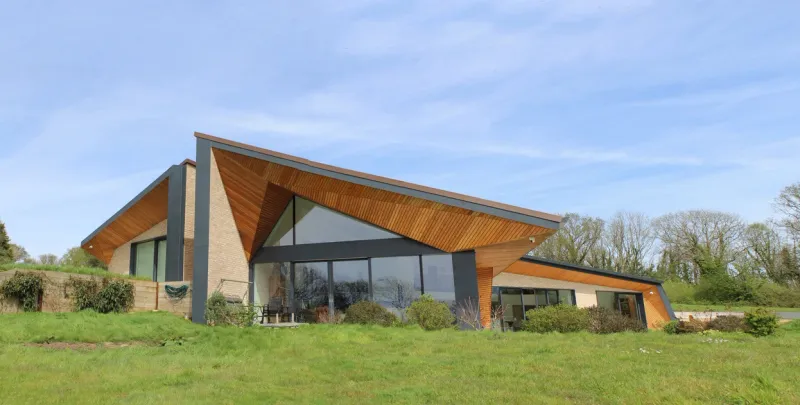 Weald House seen across its lawn, with a bold asymmetric timber-lined roof over brick walls and large glazing.