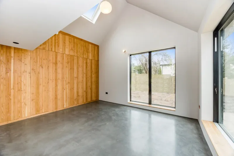 A bright finished room with a timber-clad storage wall, a vaulted ceiling, a rooflight and views to the garden.