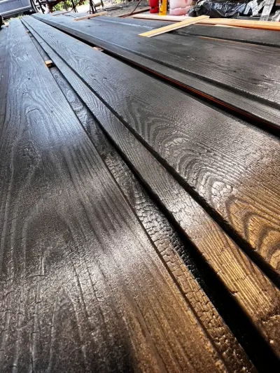 Finished shou sugi ban boards: charred timber with a glossy blackened surface and raised grain, stacked ready to install.