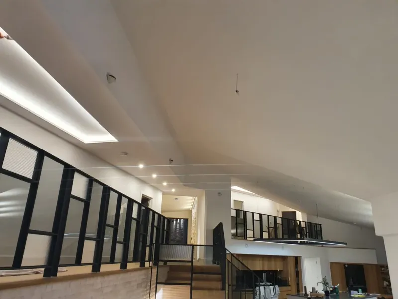 An open-plan new-build interior with a vaulted white ceiling, black-framed glazed partitions and a bespoke staircase.